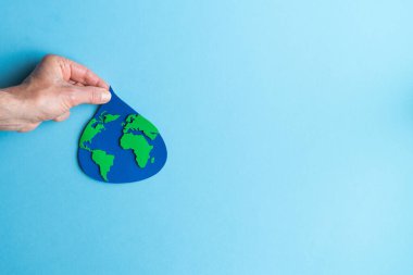 Mavi arka planda dünya haritası olan kağıttan kesilmiş bir su damlasını tutan el. Boşluğu kopyala.