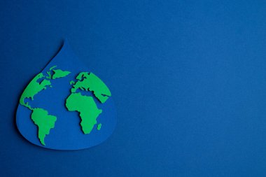 Su damlası kağıda dökülmüş, dünya haritası koyu mavi arka planda. Uzayı kopyala Üst görünüm.