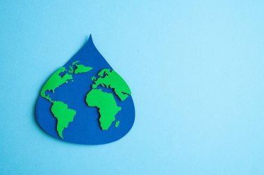 Su damlası, açık mavi arkaplanda dünya haritası ile kağıda dökülmüş. Uzayı kopyala Üst görünüm.