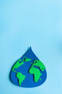 Water drop cut out on paper with world map on light blue background. Copy space. Vertical photo. Top view.