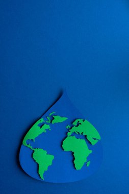 Su damlası kağıda dökülmüş, dünya haritası koyu mavi arka planda. Uzayı kopyala Üst görünüm.