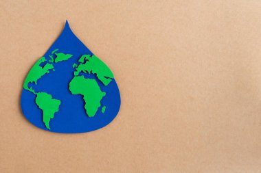 Su damlası mavi kağıttan kesilmiş ve kahverengi kart arkaplanda dünya haritası var. Boşluğu kopyala.