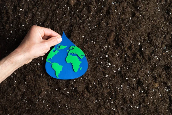 Kağıt, içinde dünya haritası olan su damlasını doğal zemin zemininde elle tutuyor. Boşluğu kopyala.