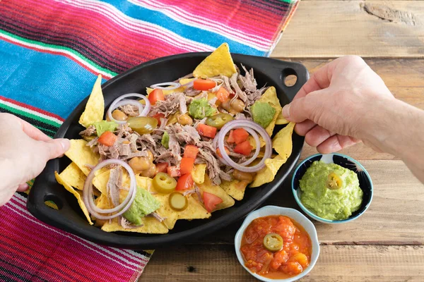 Eller, bir tepsi etli nacho 'dan yiyecek alıyor. Salsa soslu kâseler. Uzayı kopyala Meksika mutfak konsepti.
