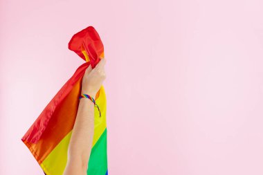 El ve LGBTQ + renkli bileklik pembe arka planda gay bayrağı gösteriyor. Boşluğu kopyala.