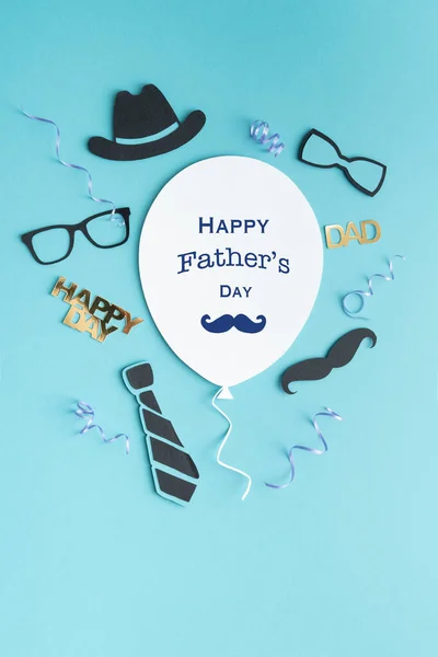 Father's Day greeting balloon card with symbols decoration on paper on blue background. Copy space. Vertical photo.