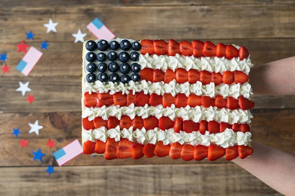 Ahşap arka planda Amerikan bayrağı renkleriyle süslenmiş kare pasta servis eden kadın elleri. Bağımsızlık Günü kutlaması. Üst görünüm.