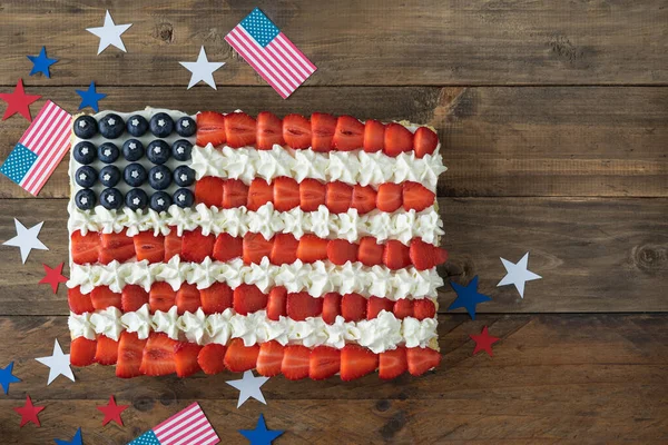 Cake with the colors of the US flag on a wooden background with flags and stars decoration. Copy space. Independence Day Celebration. Top view.
