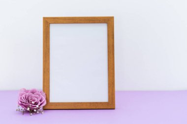 White picture with wooden frame for message on white and purple background with purple rose. Copy space.