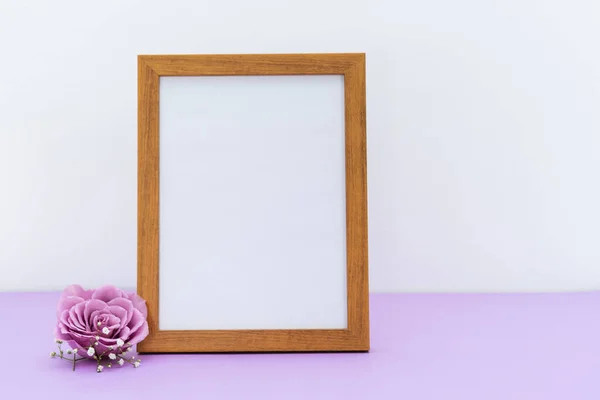 White picture with wooden frame for message on white and purple background with purple rose. Copy space.