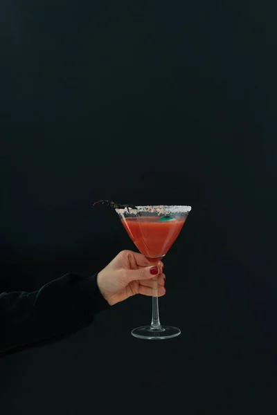 Woman's hand holds scary red cocktail with Halloween decoration on black background. Copy space. Vertical photo.