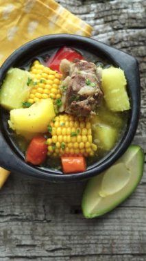 Typical Colombian Sancocho in a black ceramic bowl on a rustic wooden background. Vertical video. Top view.