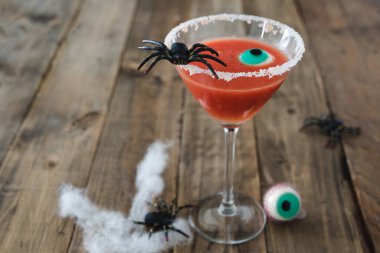 Terrifying red cocktail with spider on wooden background for Halloween with decoration. Photo vertical. Copy space.