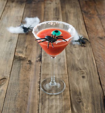 Terrifying red cocktail with spider on wooden background for Halloween with decoration. Photo square format. Copy space.