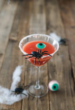 Terrifying red cocktail with spider on wooden background for Halloween with decoration. Vertical photo. Copy space.