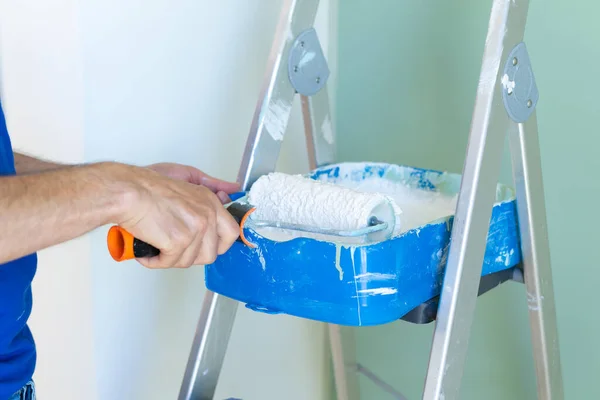 Painter\'s ladder and hand wringing paint roller. Interior of the house. Man painting the house, close-up shot.