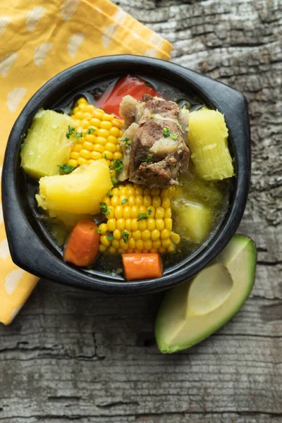 Sancocho, typical Colombian food in a black ceramic bowl on a rustic wooden background. Copy space. Top view.