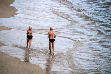 Benidorm, Alicante, İspanya - 9 Ekim 2021: İnsanlar Benidorm 'da güneşli bir sonbahar gününde sahilde güneşlenip yürüyorlar.