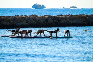 Santa Pola, Alicante, İspanya - 16 Ekim 2021 İspanya 'nın güneşli bir gününde sörf tahtasında yoga yapan bir grup insan