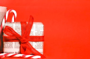 Madrid, İspanya - 12 Kasım 2021: Kırmızı arka planda kırmızı yay ve iple eski gazetelere sarılı hediyeler