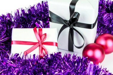 Beyaz arka planda Noel süslemesinin yanında beyaz kağıt, pembe ve siyah fiyonklarla sarılı hediyeler