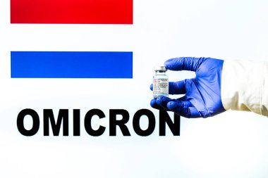 Madrid, İspanya... 29 Kasım 2021 Moderna covid aşısıyla el ele tutuşma şişesi. Arkaplanda Hollanda bayrağı ve Omicron covid değişken sözcüğü yazılı