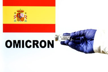 Covid aşıyla el ele tutuşma şişesi. İspanyol bayrağı ve Omicron covid değişkeni arka planda yazıldı