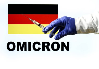 El ele tutuşma şırıngası ve covid aşısı. Alman bayrağı ve Omicron covid değişkeni arka planda yazıldı