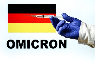 El ele tutuşma şırıngası ve covid aşısı. Alman bayrağı ve Omicron covid değişkeni arka planda yazıldı