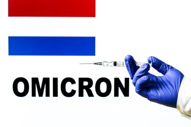 El ele tutuşma şırıngası ve covid aşısı. Arkaplanda Hollanda bayrağı ve Omicron covid değişken sözcüğü yazılı