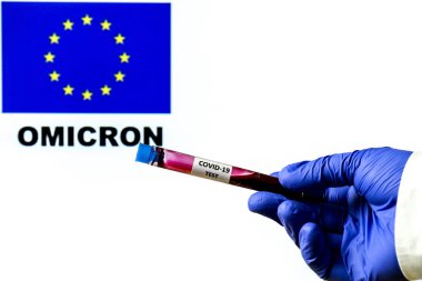 Üzerinde Avrupa bayrağı ve Omicron kelimesi yazılı beyaz zemin üzerinde covid-19 virüsünün el ele tutuşma tüpü.