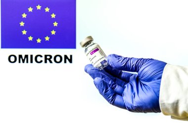 Madrid, İspanya... 29 Kasım 2021 Astrazeneca covid aşısıyla el ele tutuşma şişesi. Arka planda yazılan Avrupa bayrağı ve Omicron covid değişkeni