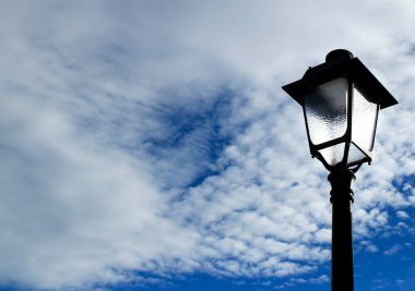 Bulutlu gökyüzünün altında klasik sokak lambası direği. Tek renkli resim.