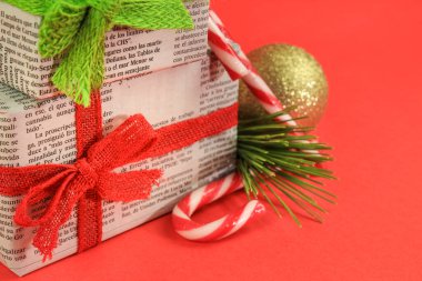 Madrid, İspanya - 17 Aralık 2021: Çam dalı, Noel tatlısı ve kırmızı arka planda altın toplarla eski gazetelere sarılı hediyeler