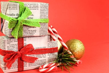Madrid, İspanya - 17 Aralık 2021: Çam dalı, Noel tatlısı ve kırmızı arka planda altın toplarla eski gazetelere sarılı hediyeler