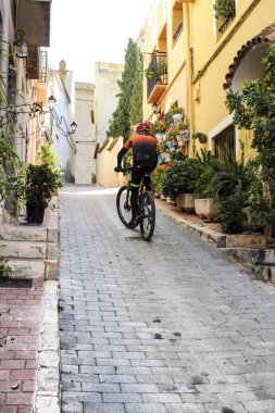 Polop, Alicante, İspanya... 28 Kasım 2021: Bisikletçi Polop 'un Narrow Caddesi boyunca dik tepeye çıkıyor.