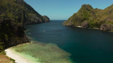 Kumsalı ve kayalıklarla çevrili berrak mavi suyu olan tropik hava aracı peyzajı. El nido, Filipinler, Palawan. Tropikal kayalık adaları, okyanus mavisi suları olan deniz burnu. Yaz ve seyahat