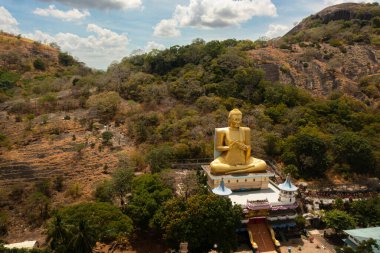 A statue of a seated golden Buddha on a rock in a mountain temple. Sri Lanka.