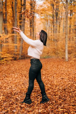 Güzel kız güler, zıplar ve sonbahar mevsiminde ormanda yapraklarla oynar..