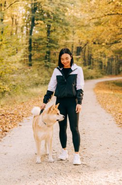 Sonbahar boyunca ormanda evcil köpeğini gezdiren mutlu bir kızın portresi. Akita inu 'nun yaşamı.