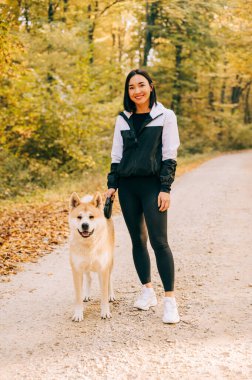 Sonbahar boyunca ormanda evcil köpeğini gezdiren mutlu bir kızın portresi. Akita inu 'nun yaşamı.