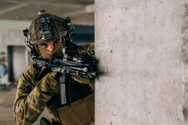 Multicam üniformalı özel kuvvetler operatörü ve saldırı tüfeği HK 416 terk edilmiş binada CQB savaş eğitimi alırken. Kentsel çevrede çakal kahverengi ve MC dişlisi.