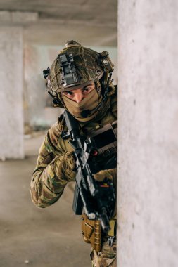 Multicam üniformalı özel kuvvetler operatörü ve saldırı tüfeği HK 416 terk edilmiş binada CQB savaş eğitimi alırken. Kentsel çevrede çakal kahverengi ve MC dişlisi.
