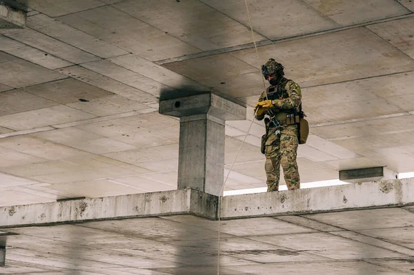 Special forces operator rappeling down the abandoned building on the rope. Multicam camo with coyote brown addons.