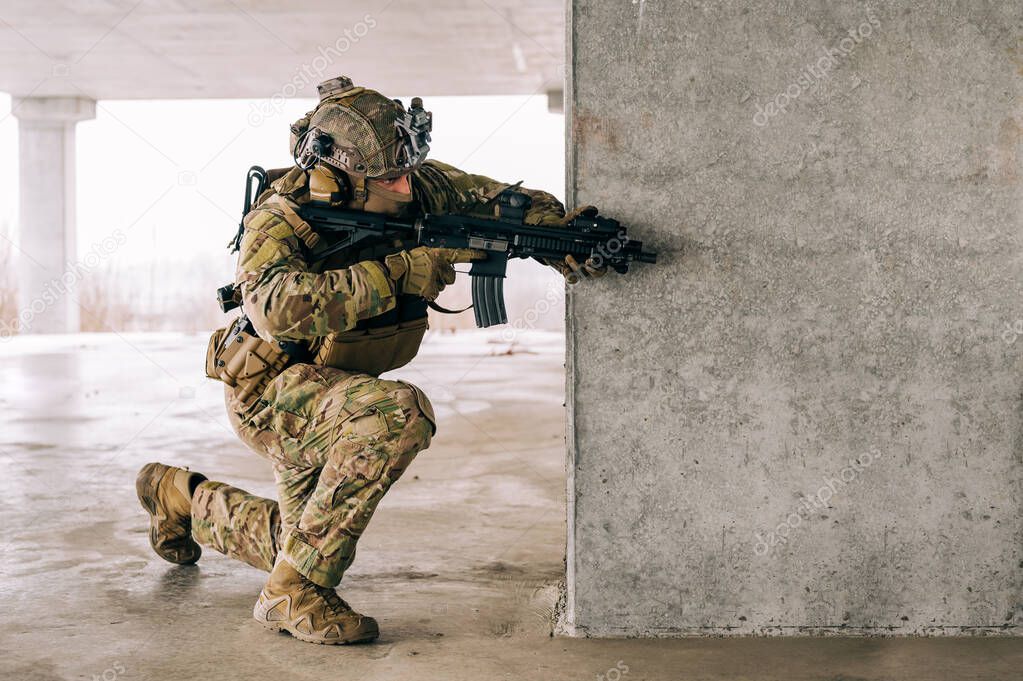 Special forces operator wearing Multicam uniform and his assault rifle HK 416 while practicing CQB combat training in the abandoned building. Coyote brown and mc gear in the urban environment.