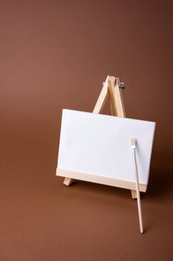 Küçük bir ahşap sehpada beyaz tuval kahverengi zeminde asgari konsept olarak duruyor. Boş boş çerçeve, kopyalama alanı olan tasarım için..