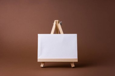 Küçük bir ahşap sehpada beyaz tuval kahverengi zeminde asgari konsept olarak duruyor. Boş boş çerçeve, kopyalama alanı olan tasarım için..