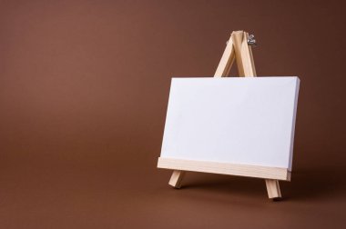 Küçük bir ahşap sehpada beyaz tuval kahverengi zeminde asgari konsept olarak duruyor. Boş boş çerçeve, kopyalama alanı olan tasarım için..