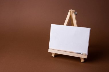 Küçük bir ahşap sehpada beyaz tuval kahverengi zeminde asgari konsept olarak duruyor. Boş boş çerçeve, kopyalama alanı olan tasarım için..