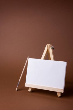 Küçük bir ahşap sehpada beyaz tuval kahverengi zeminde asgari konsept olarak duruyor. Boş boş çerçeve, kopyalama alanı olan tasarım için..